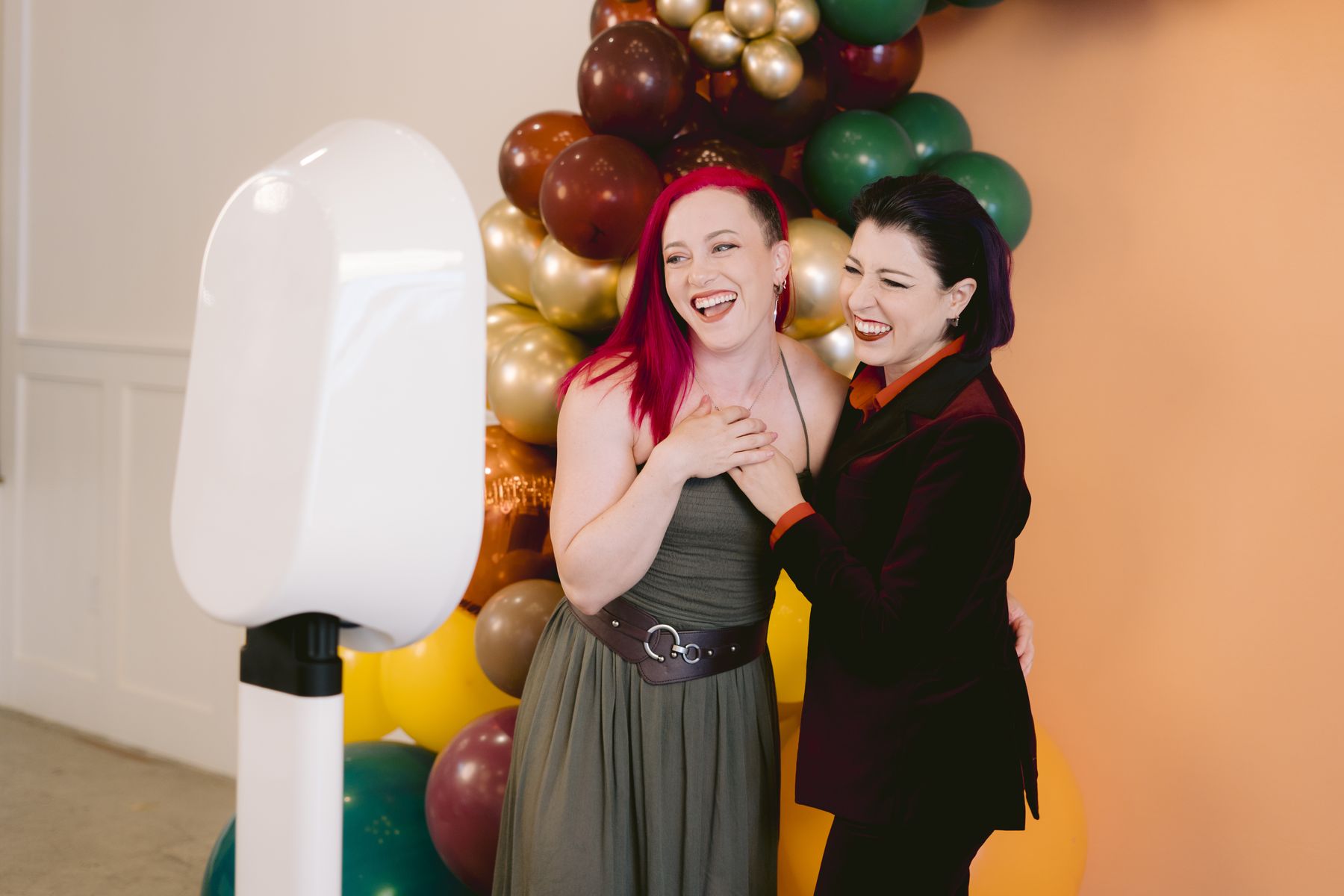 Two guests laughing beside the EVNT Booth digital photo booth at a party